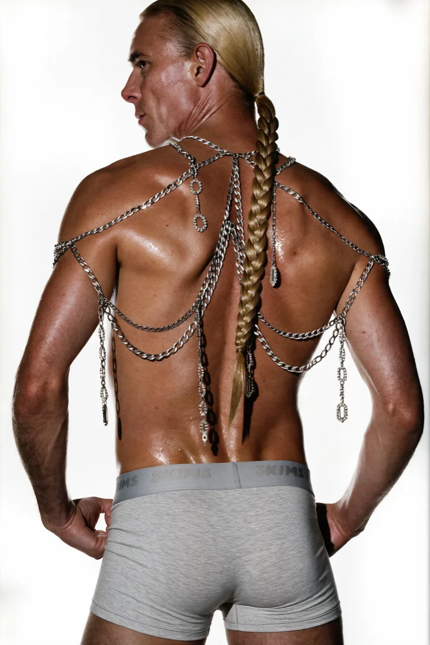 Model photographed from behind in grey boxers, a curb-chain harness with crystal drops across the shoulders