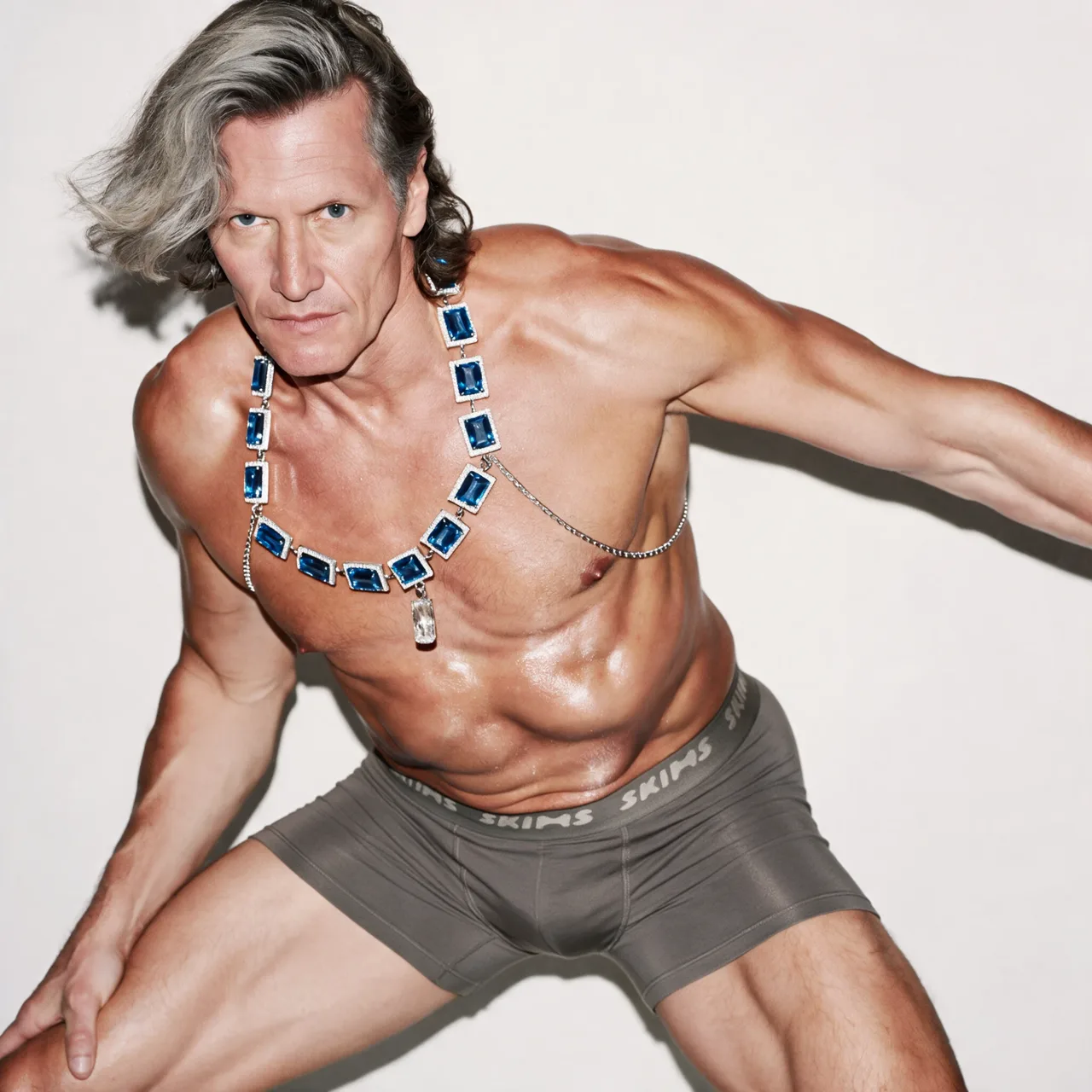 Model lunging in grey boxers, wearing a blue gem collar and a fine waist chain