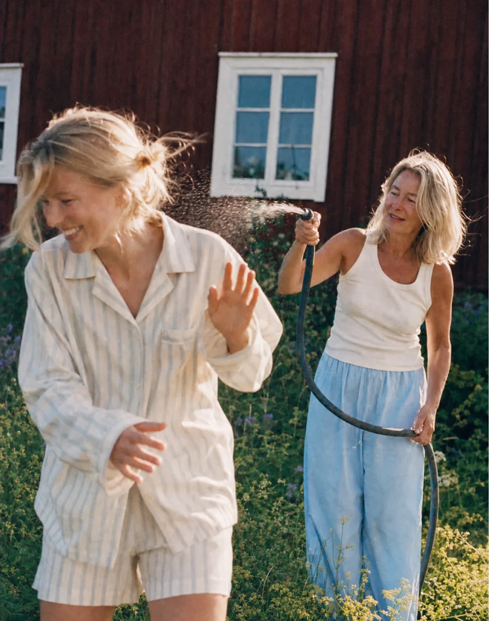 Two women laughing as one sprays a garden hose outside the cabin