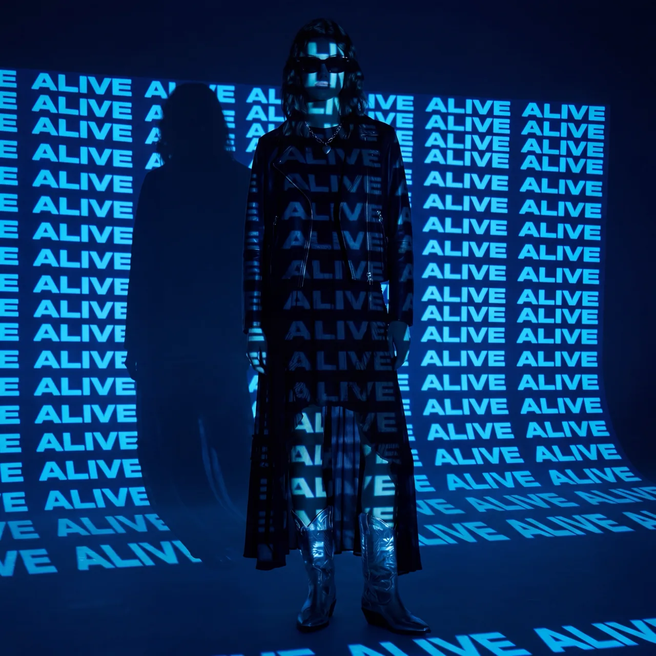 AllSaints: a model in a biker jacket, long black dress and silver cowboy boots in a blue ALIVE projection, AI concept work