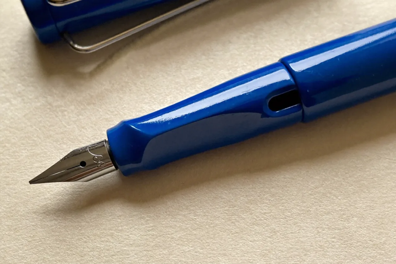 A blue fountain pen with a steel nib resting on cream paper, its cap and wire clip behind, AI concept work