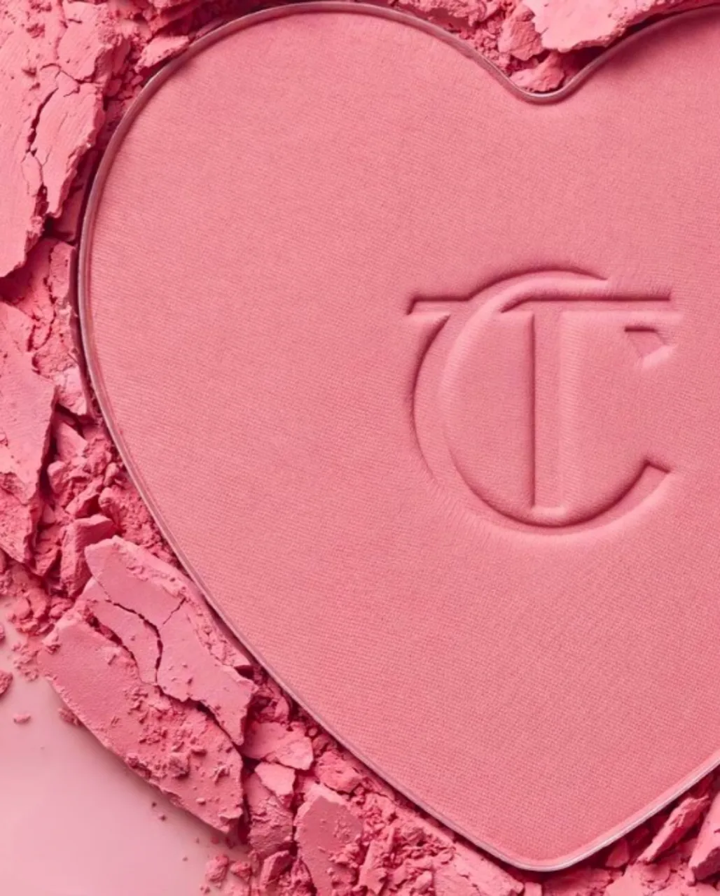 Charlotte Tilbury: macro of a heart-shaped pink blush pressed with the CT monogram, crushed powder round it, AI concept work