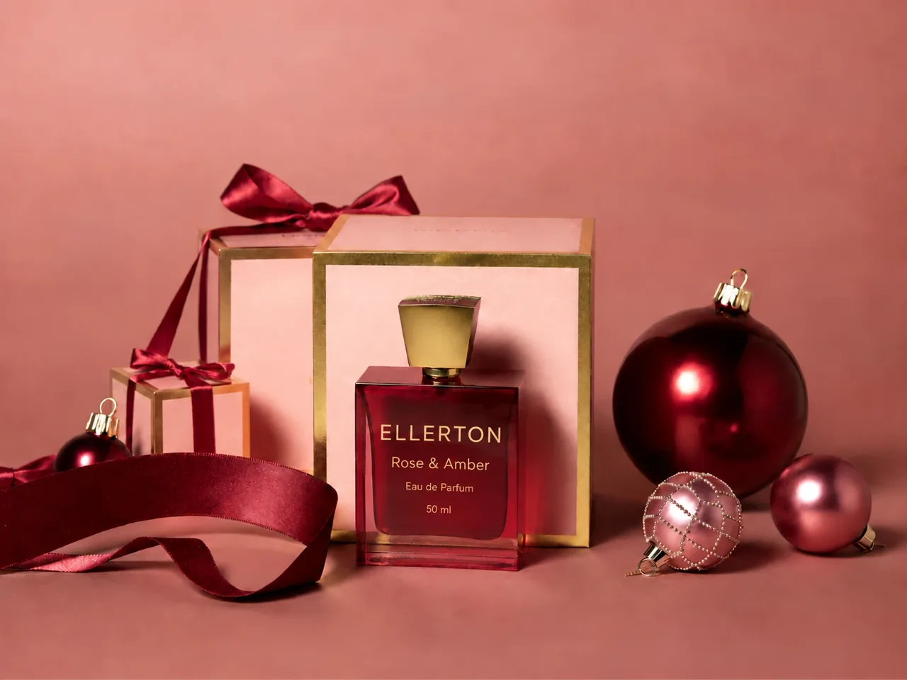 Christmas product photography concept: a burgundy eau de parfum bottle in front of its blush box, with gift boxes, satin ribbon and baubles in matching colours