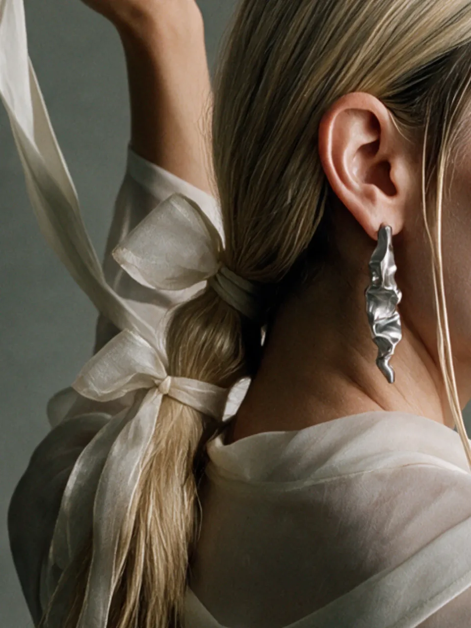 Completedworks concept: a crumpled silver earring on a model's ear, her ponytail tied with sheer organza bows