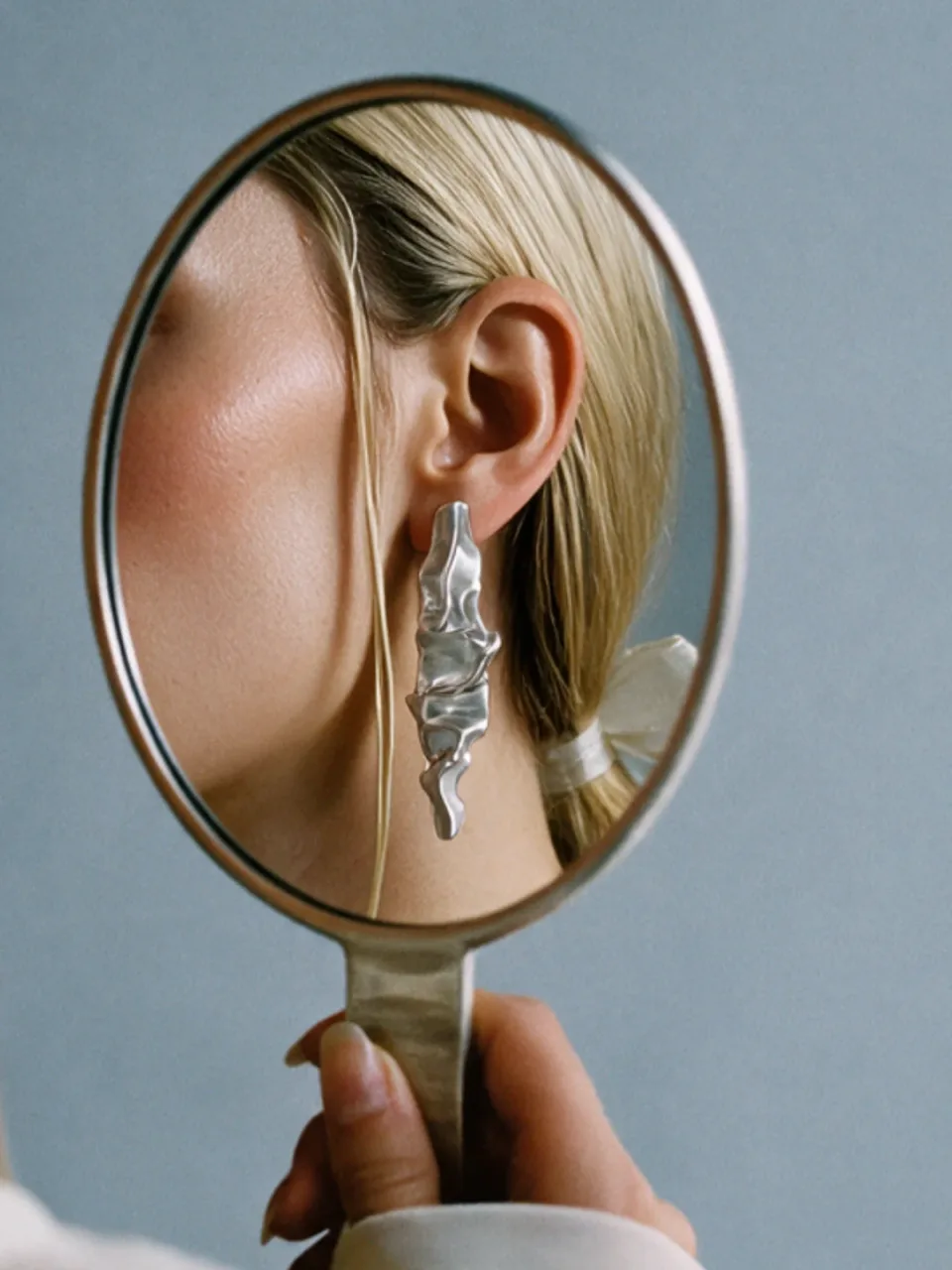 Completedworks concept: a hand mirror reflects a model's ear and her crumpled silver earring