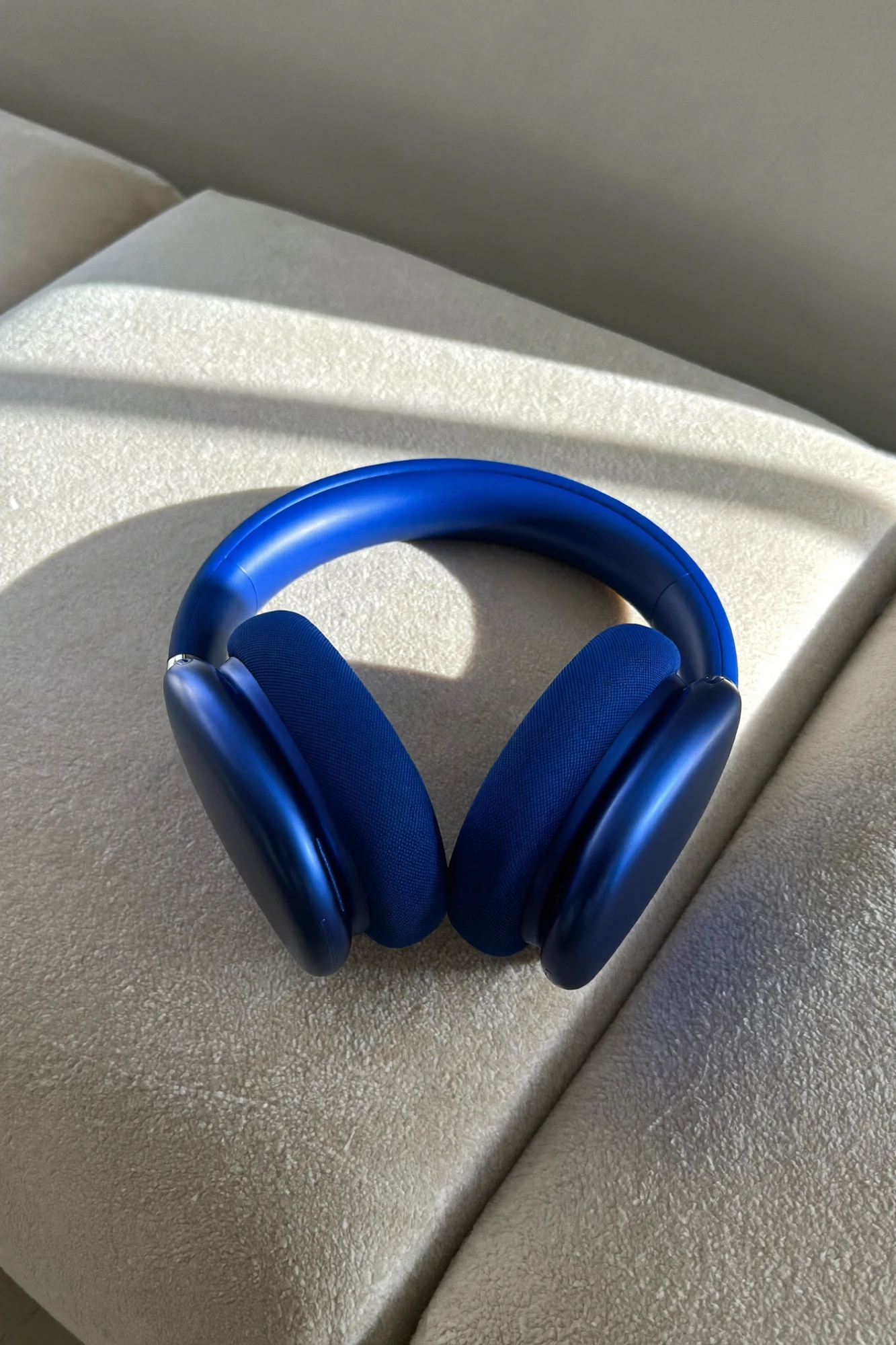 Electric-blue concept headphones resting on a cream textured sofa in low sunlight, a band of shadow across them