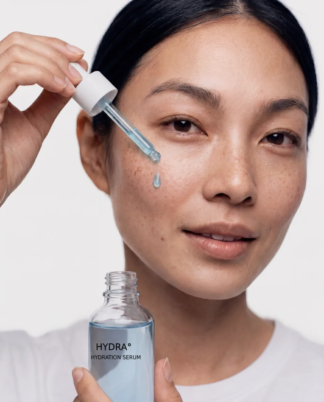 A freckled woman lets a drop of HYDRA serum fall from the pipette onto her cheek, holding the open bottle, AI concept work