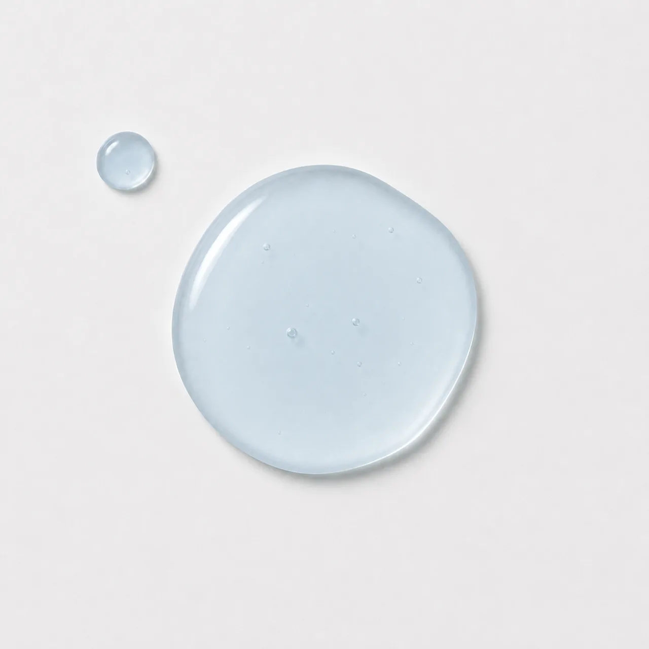 HYDRA hydration serum: a round pool of pale blue serum and one small drop beside it on a pale grey surface, AI concept work