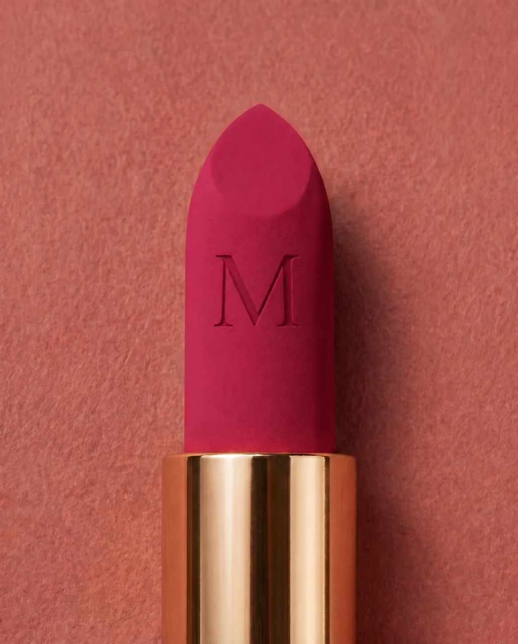 MUSE lipstick bullet in close-up: a magenta shade engraved with the M monogram, in a gold case on dusty rose, AI concept work