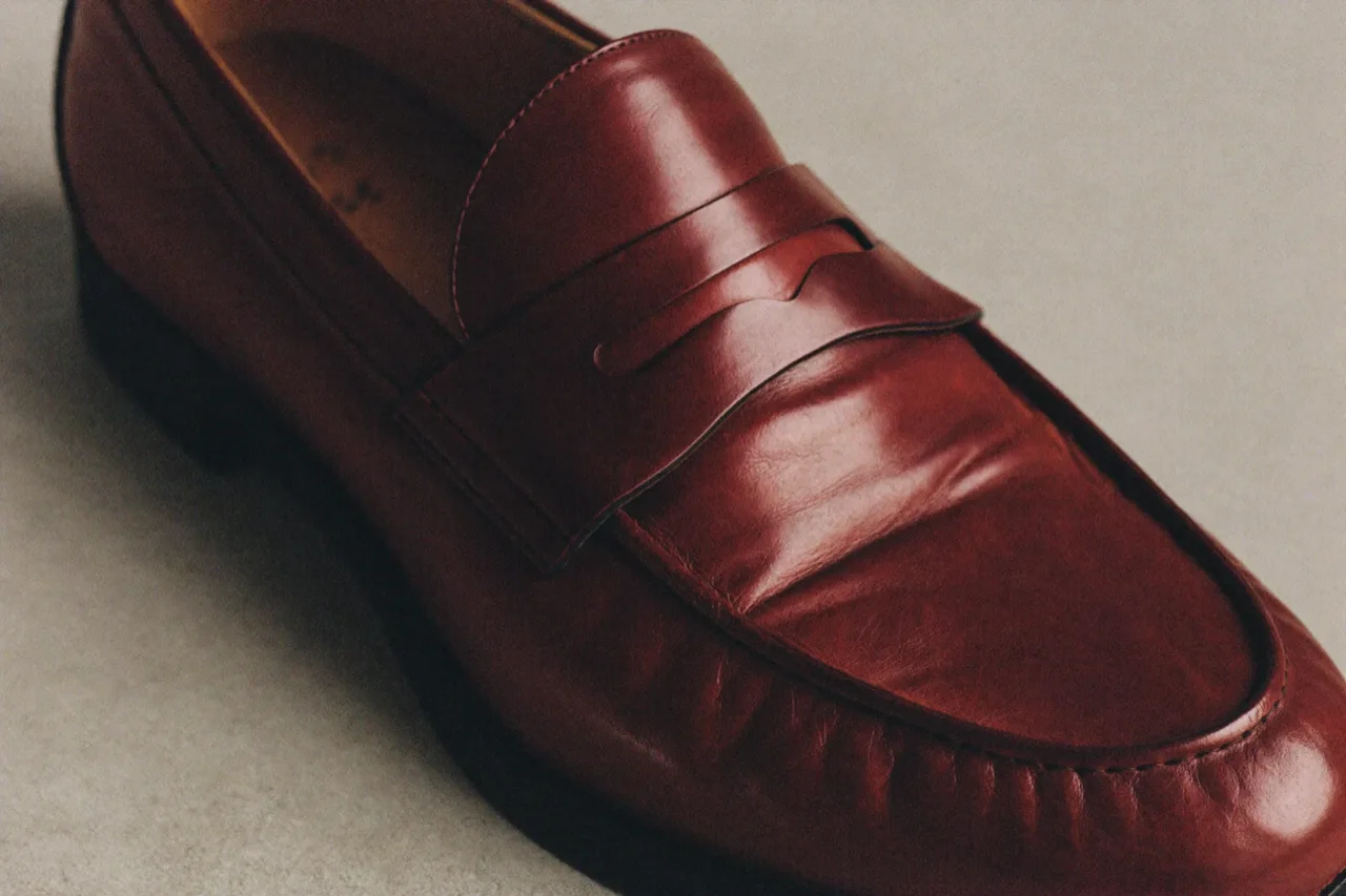 Close-up of an oxblood leather penny loafer, its strap and stitching, on a pale grey ground, AI concept work