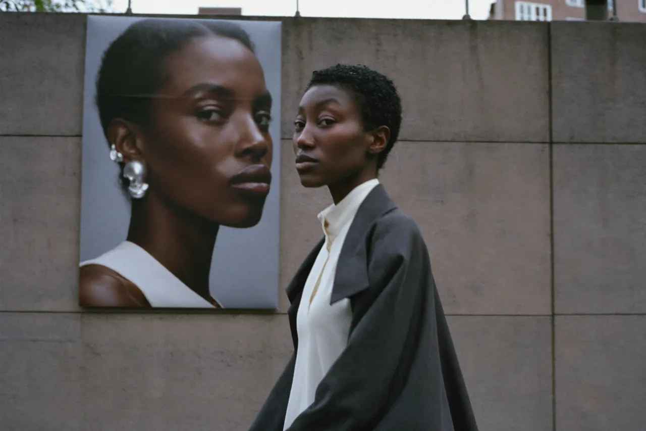 A woman in a charcoal coat walks past a large printed portrait of a model wearing a silver skull earring, AI concept work