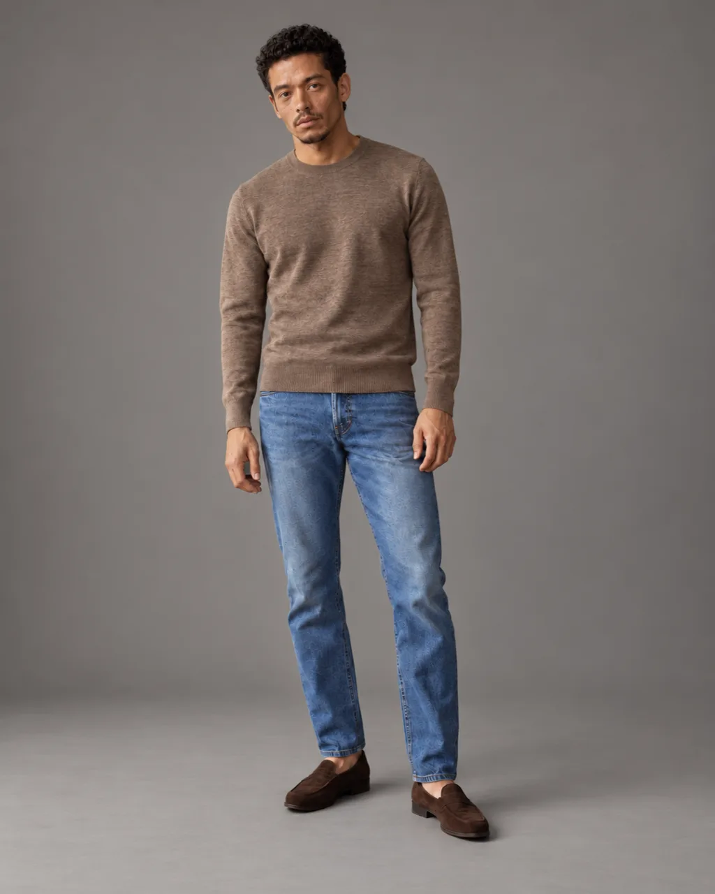 Sunderly lookbook, look 1, taupe knit and indigo jeans: full length on a plain grey ground, AI concept work