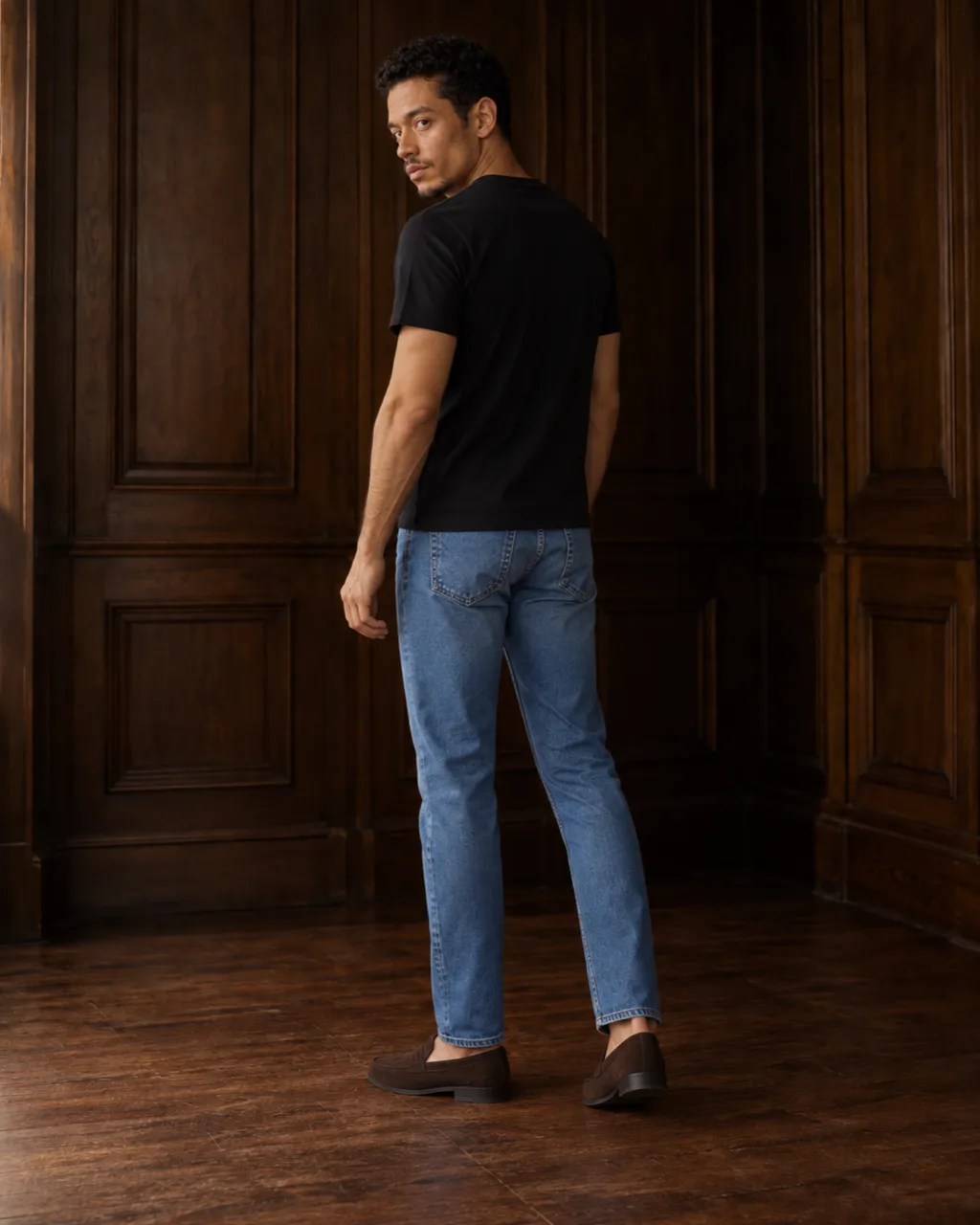 Sunderly look 2, black T-shirt and indigo jeans: from behind, three-quarter view, in a wood-panelled room, AI concept work