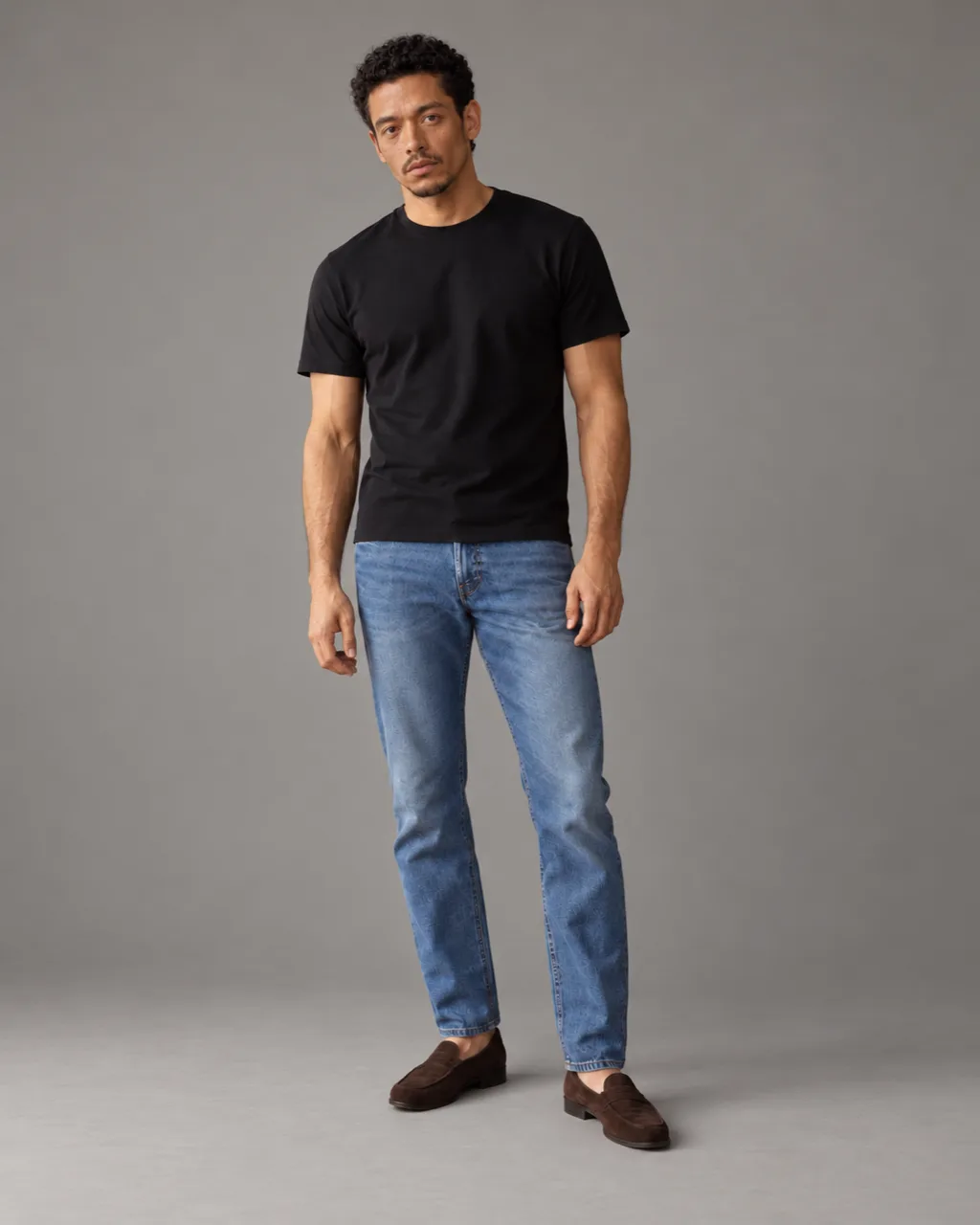 Sunderly lookbook, look 2, black T-shirt and indigo jeans: full length on a plain grey ground, AI concept work