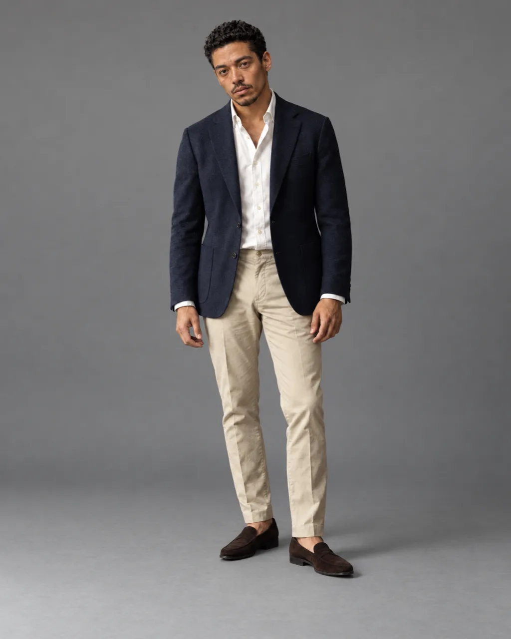 Sunderly lookbook, look 4, navy blazer, white shirt and stone chinos: full length on a plain grey ground, AI concept work