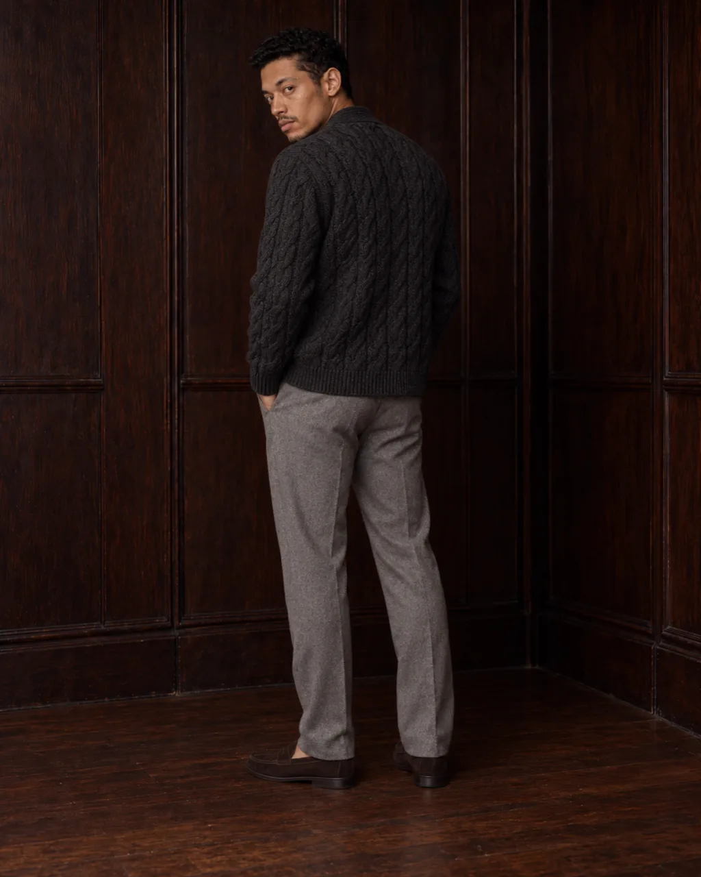 Sunderly look 6, charcoal cable cardigan and grey flannel trousers: from behind, three-quarter view, AI concept work