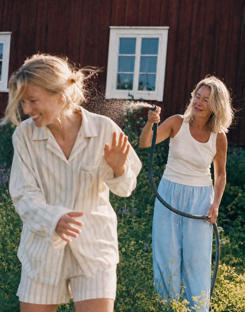 TEKLA concept: two women laughing as one sprays a garden hose outside the cabin